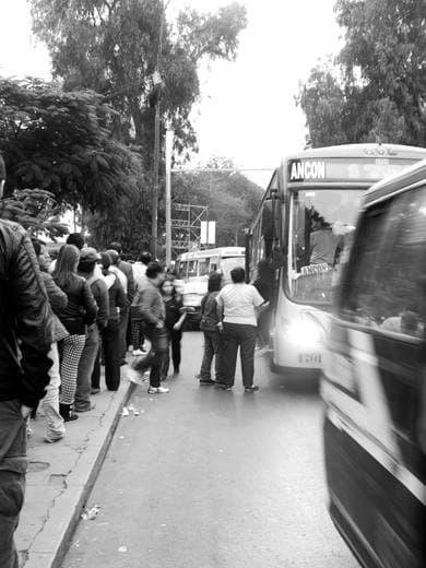 Personas esperando junto a un autobús en movimiento, blanco y negro